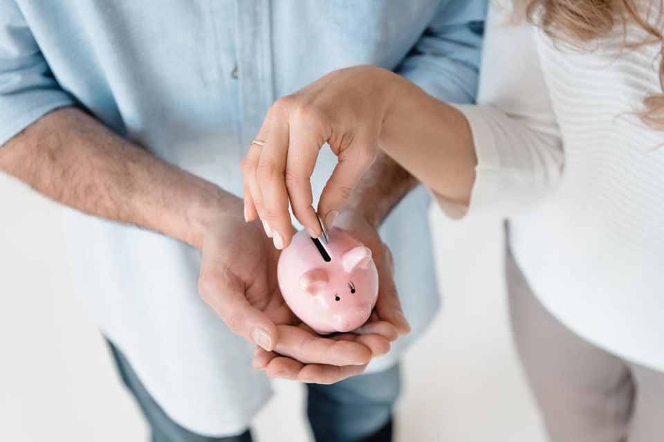 Finanzen in einer Beziehung: Das muss zum Anfang geklärt werden: Frau wirft Geld in Sparschwein