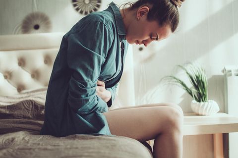Endometriose: Erfahrungsbericht über ein Leben mit Schmerzen: Frau sitzt mit Bauchschmerzen auf Bett