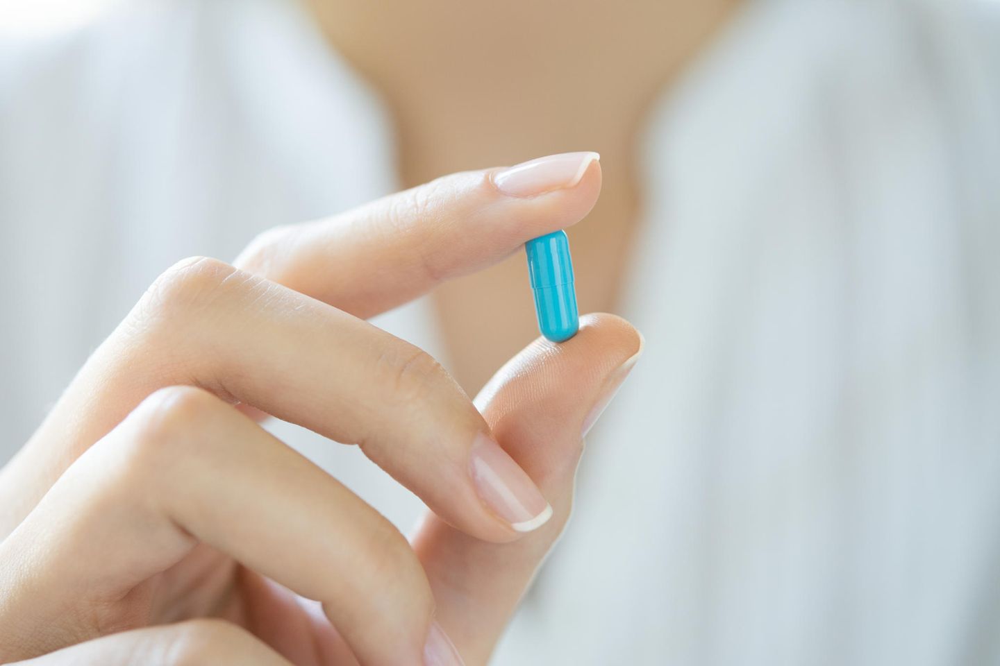 Arzt hält blaue Pille zwischen zwei Fingern