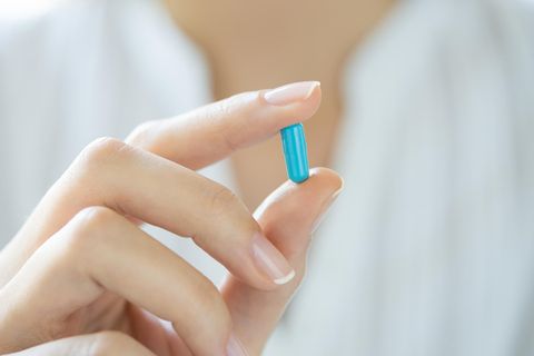 Arzt hält blaue Pille zwischen zwei Fingern