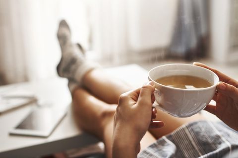 Entschleunigung: Eine Frau trinkt Tee und legt die Füße auf den Tisch