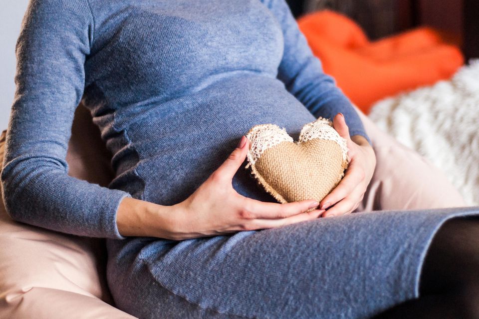Schwangere Frau mit herzförmigem Kissen auf Bauch