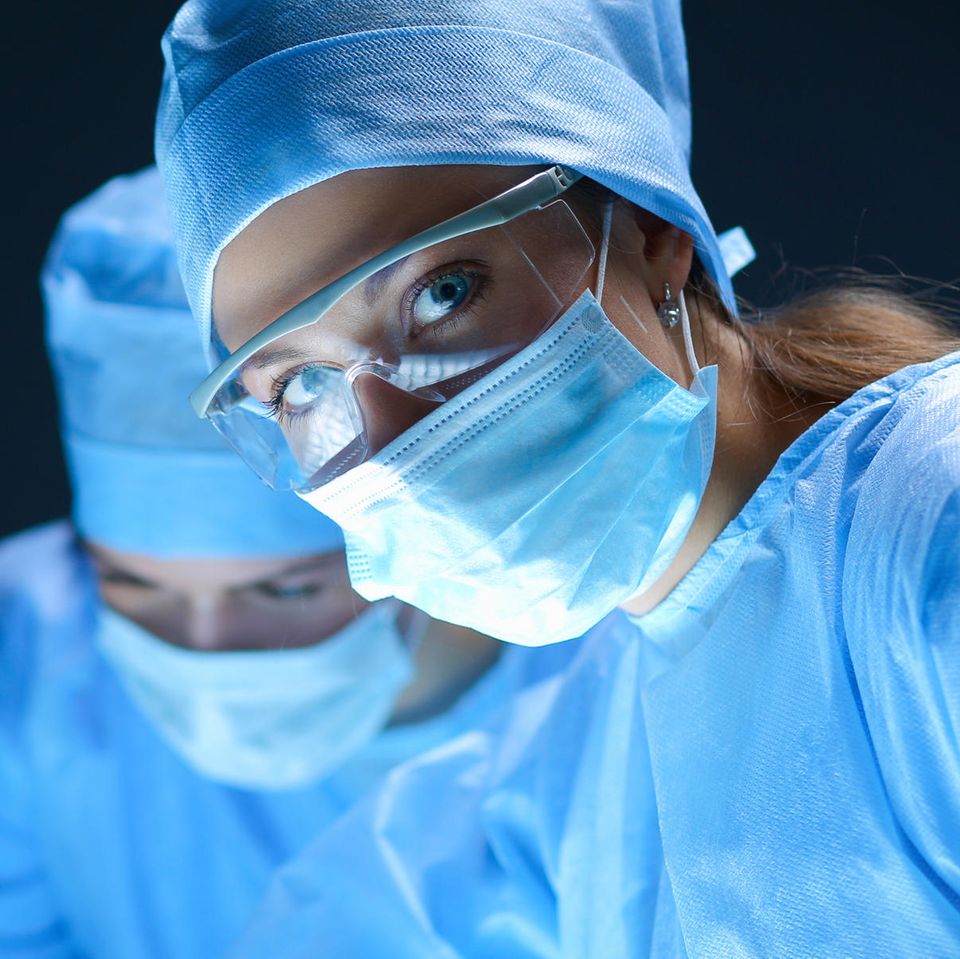 Eine Chirurgin trägt während ihrer Arbeit Mundschutz und OP-Kleidung