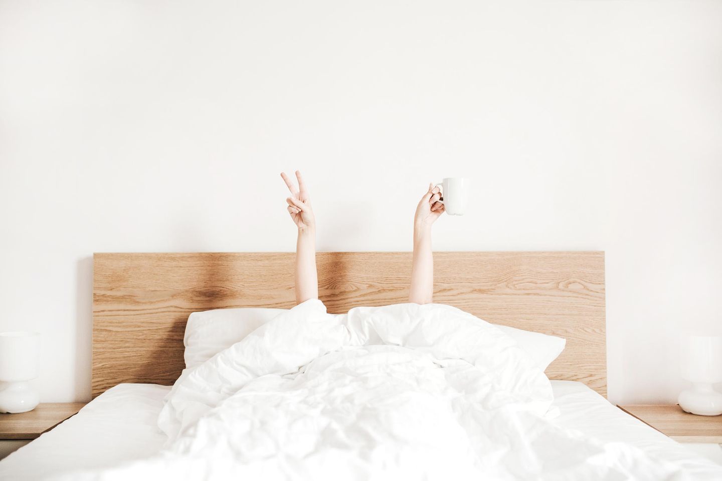 Horoskop: Eine Frau liegt im Bett und streckt nur ihre Hände in die Luft