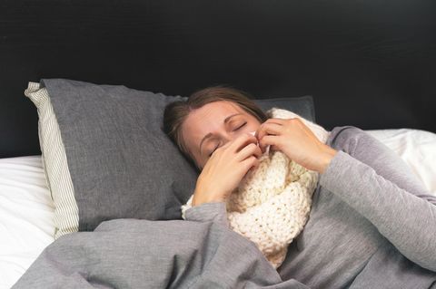 Erkältete Frau mit Schal im Bett