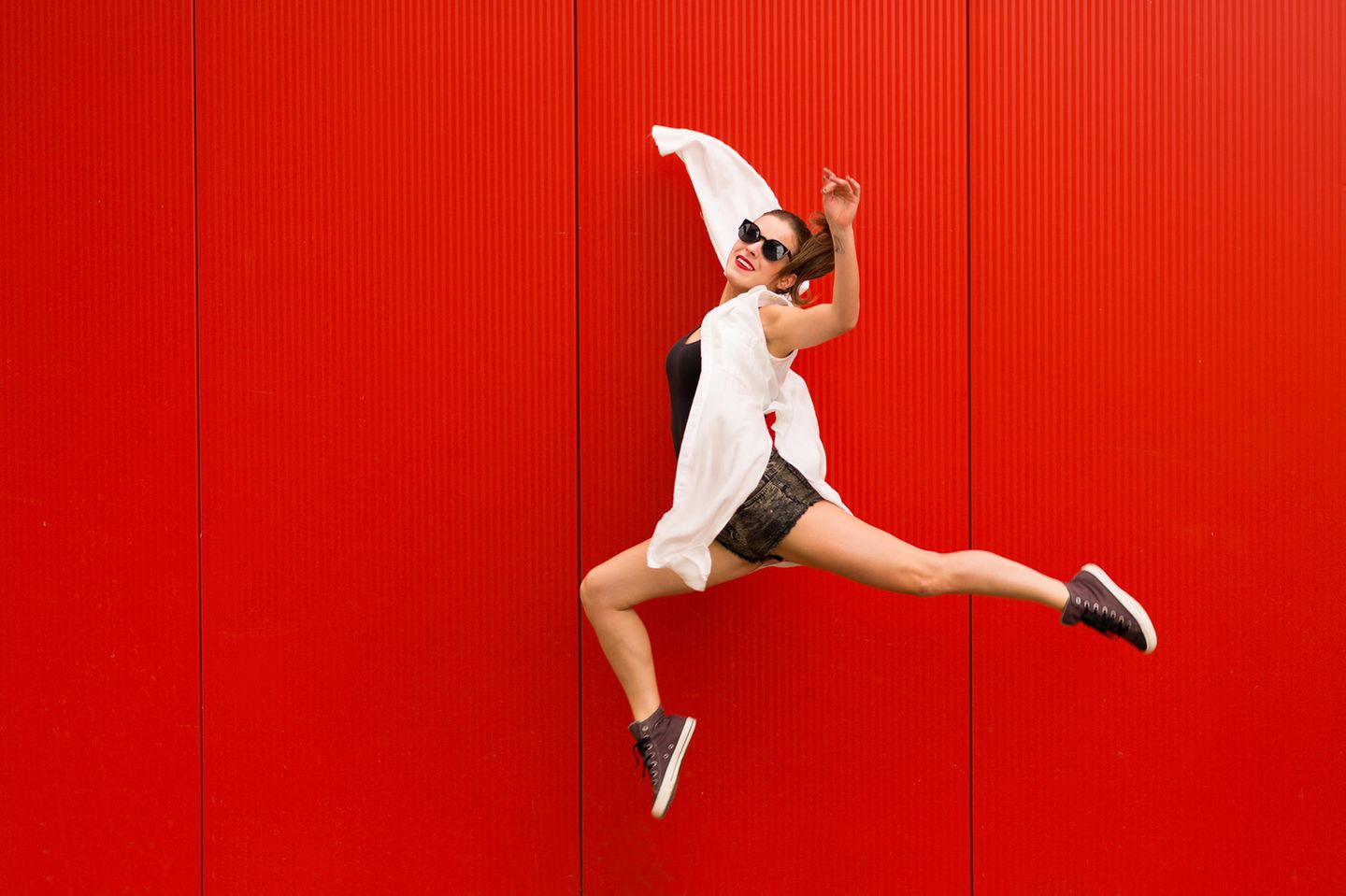 Junge Frau springt vor rotem Hintergrund in die Luft