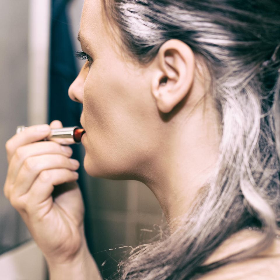 Graue Haare: Frau mit grauen Haaren trägt Lippenstift auf