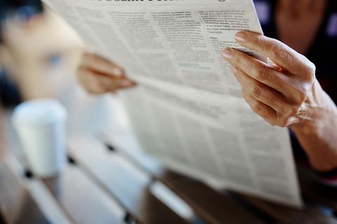 Ältere Frau liest Zeitung am Tisch