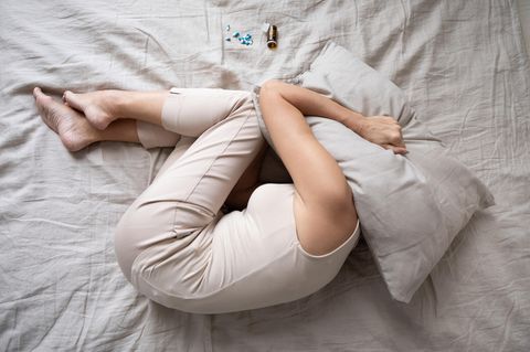 Depressive Frau im Bett mit Kissen über Kopf und Tabletten