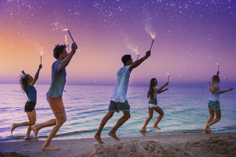Sternzeichen und die vier Elemente: Freunde laufen mit Wunderkerzen am Meer entlang