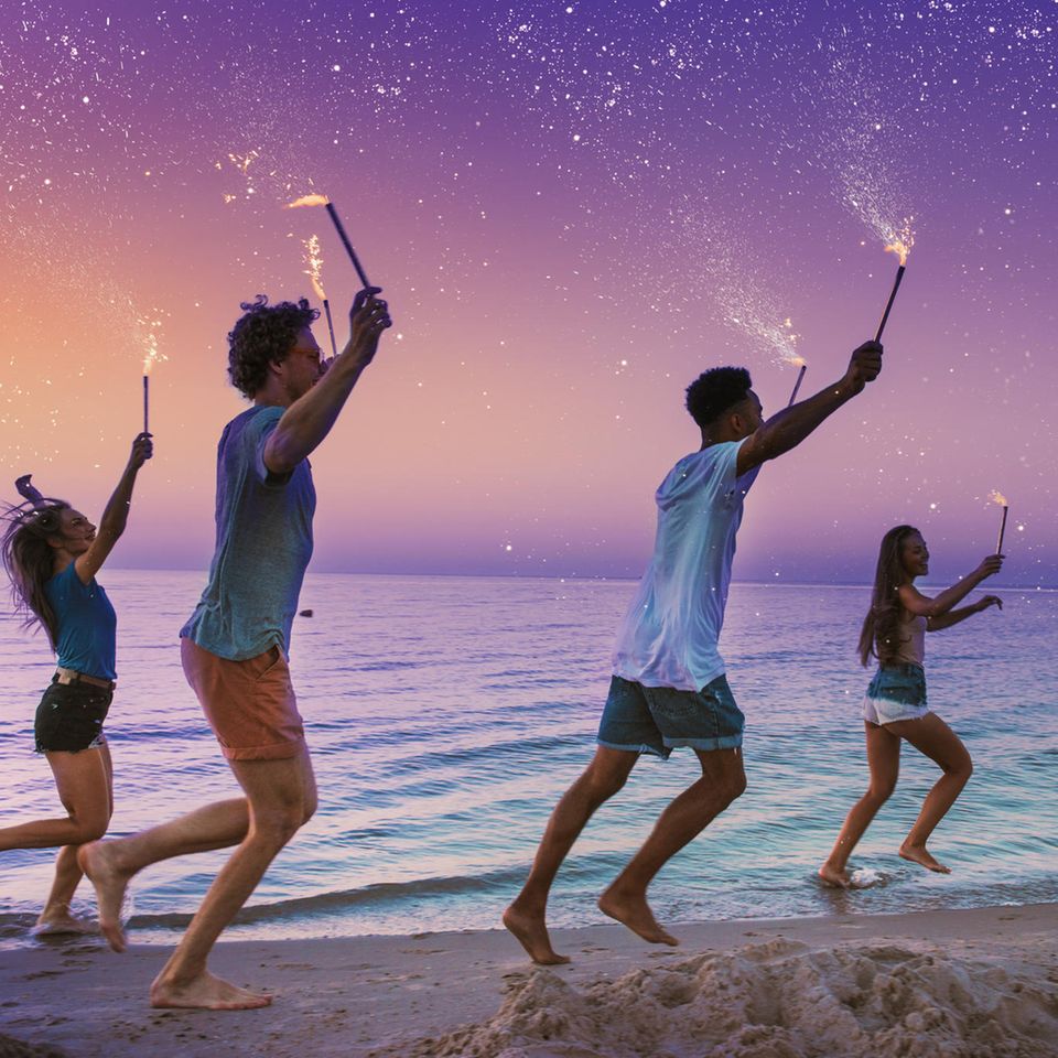 Sternzeichen und die vier Elemente: Freunde laufen mit Wunderkerzen am Meer entlang