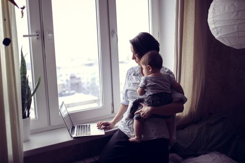 Frau am Laptop mit Kind auf Arm
