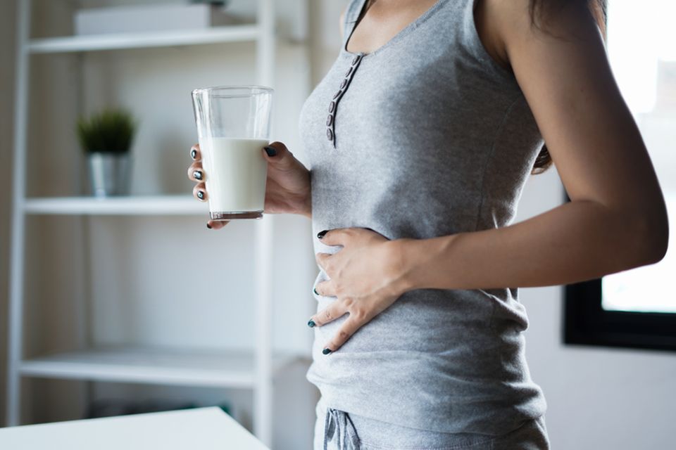 Laktoseintoleranz Symptome: Frau hält Glas mit Milch und eine Hand auf den Bauch
