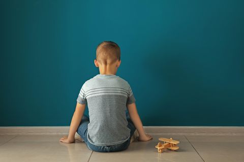 Kind mit Spielzeugflugzeug sitzt vor Wand