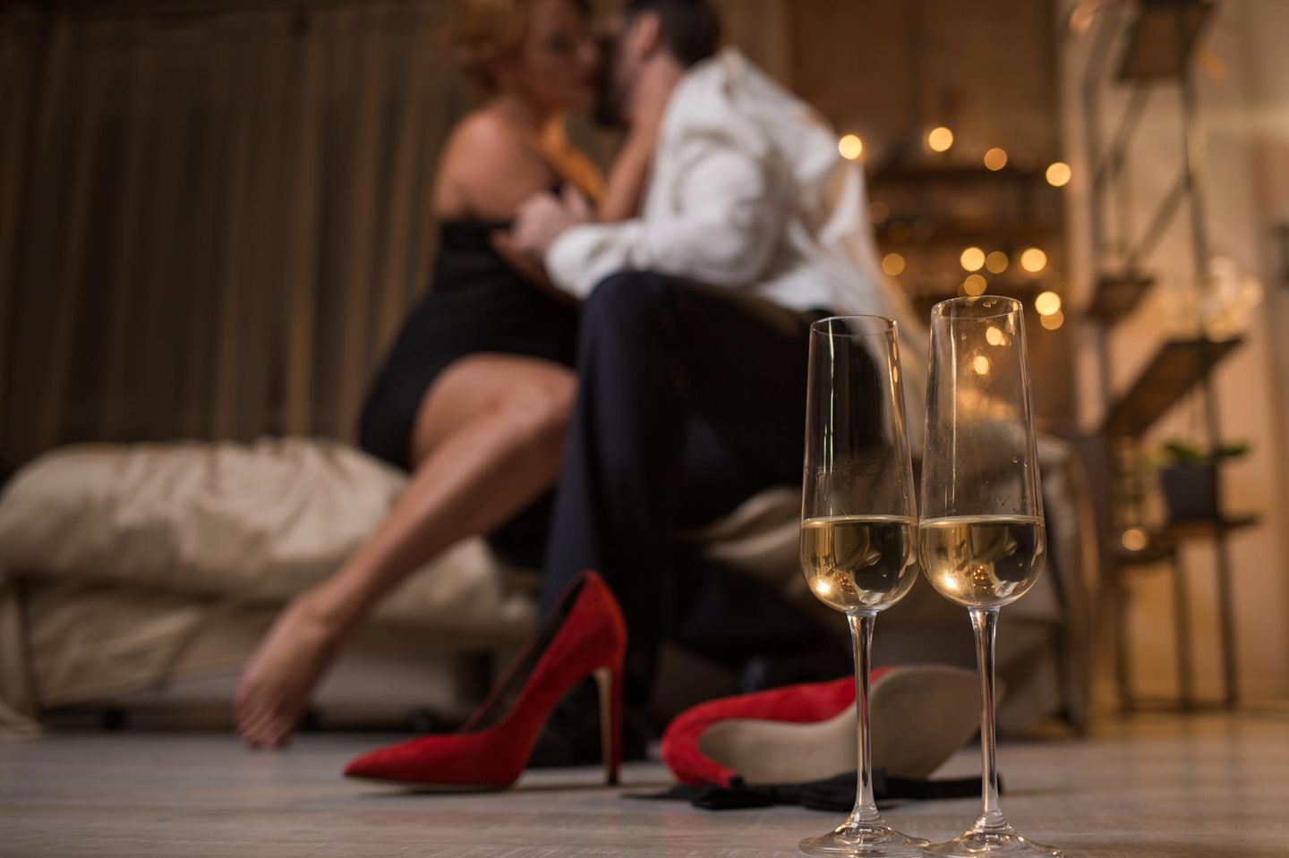 Paar auf Bett, Schuhe und Champagner im Vordergrund