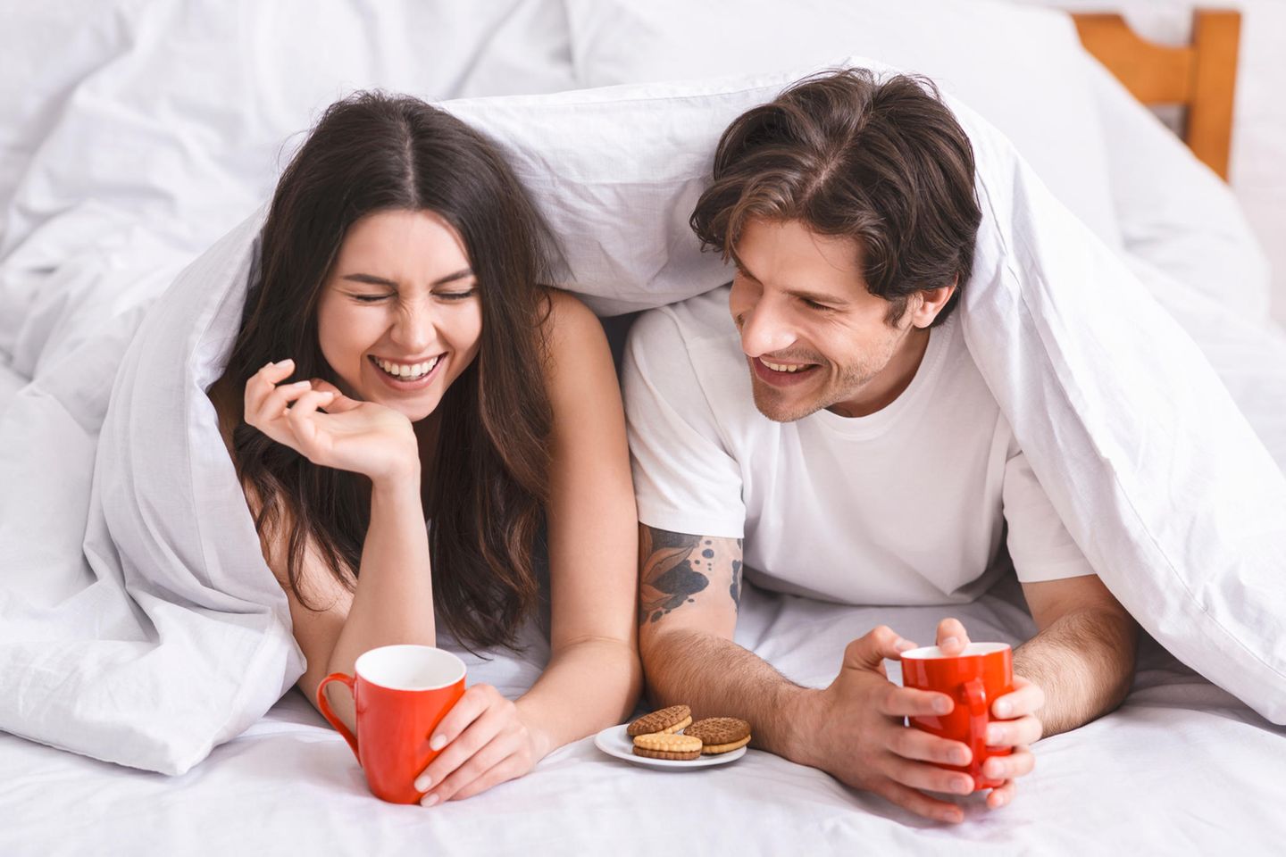 Wie trenne ich Job und Beziehung? Ein glückliches Paar liegt im Bett und lacht zusammen