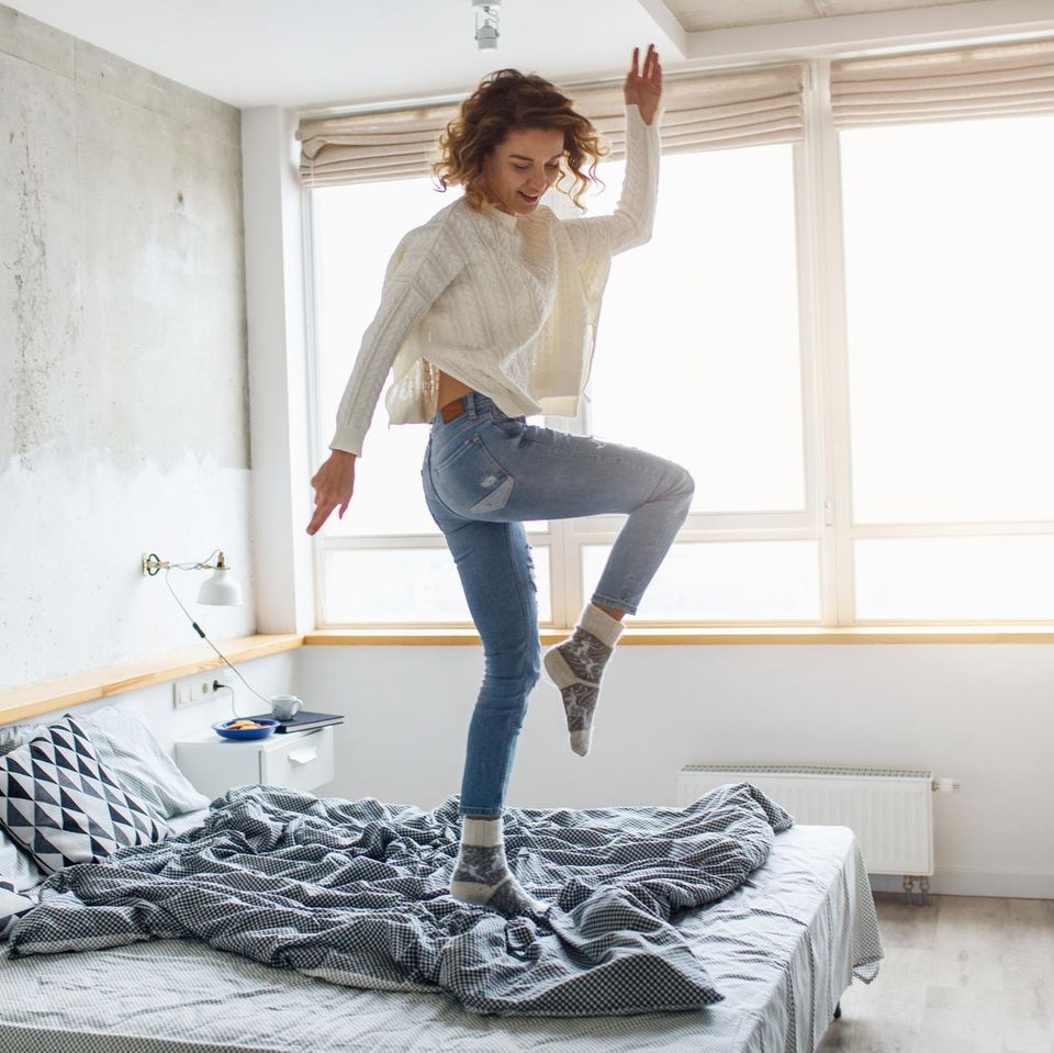 Horoskop: eine fröhliche Frau tanzt auf ihrem Bett