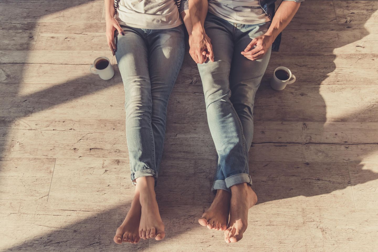 Horoskop: Ein Paar sitzt nebeneinander auf dem Boden und hält Händchen