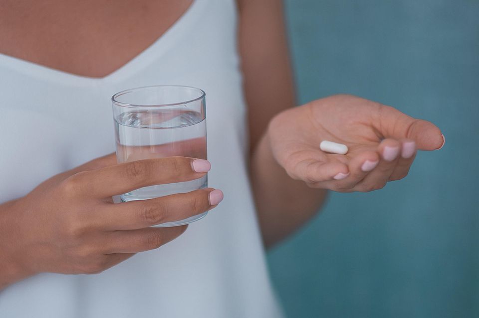 Wann Antibiotika sinnvoll sind: Frau mit einem Glas Wasser und Tablette