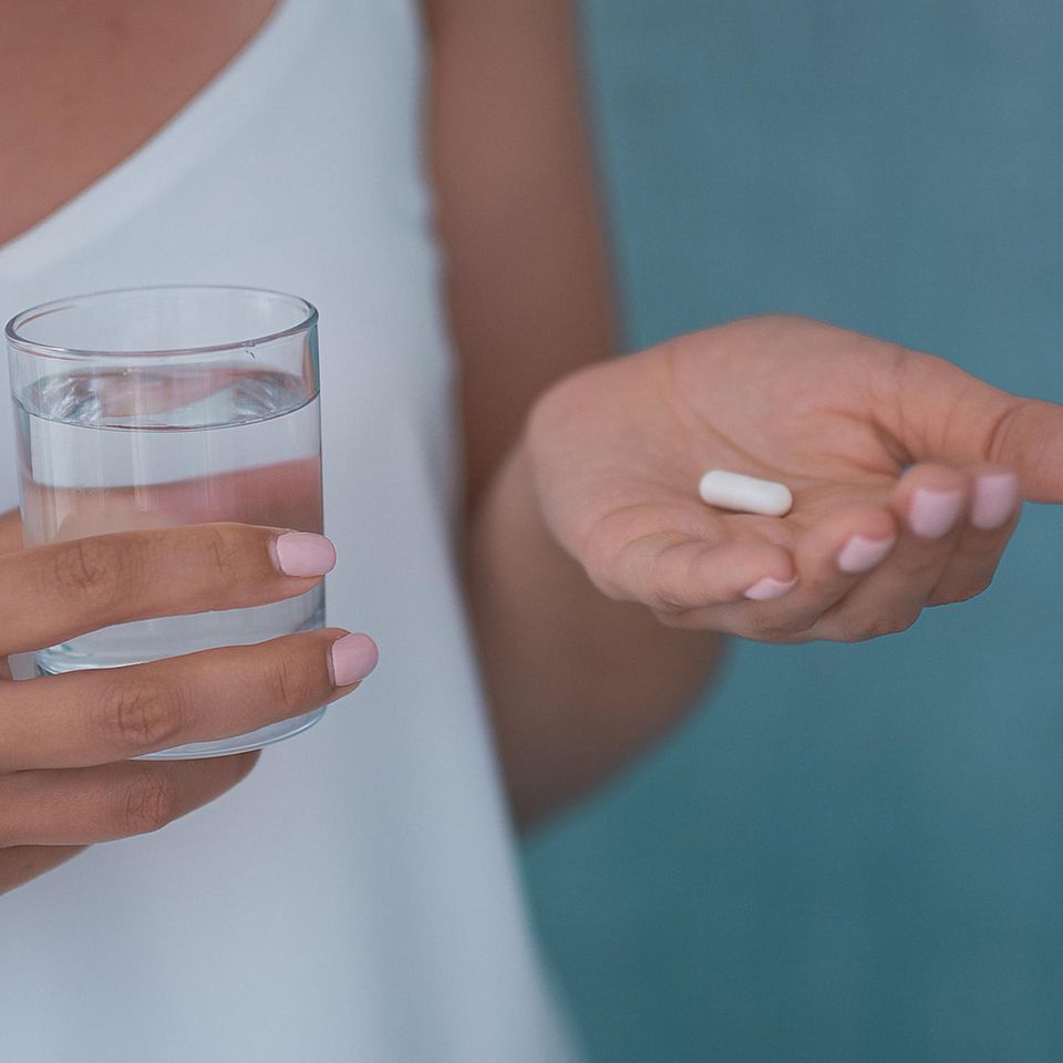 Wann Antibiotika sinnvoll sind: Frau mit einem Glas Wasser und Tablette