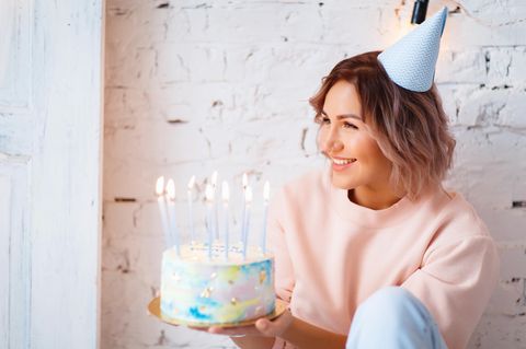 Geburtstag allein feiern: Eine glückliche Frau mit Torte und Hütchen auf dem Kopf