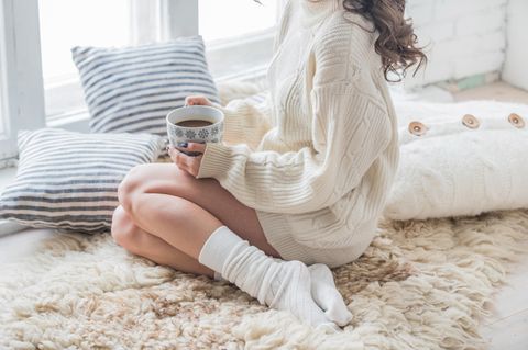 Corona-Isolation: Eine Frau sitzt allein zu Hause am Fenster und trinkt Kaffee