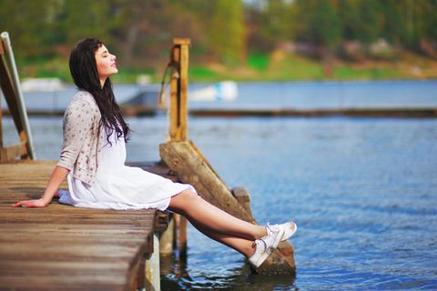 Alleine glücklich sein: Eine Frau sitzt am See und genießt die Sonne