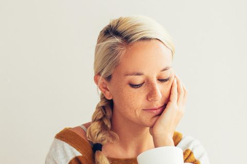 Nicht beziehungsfähig: Frau sitzt traurig mit Tasse in der Hand im Bett