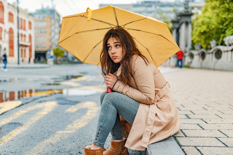 Corona aktuell: Eine nachdenkliche Frau unter einem Schirm