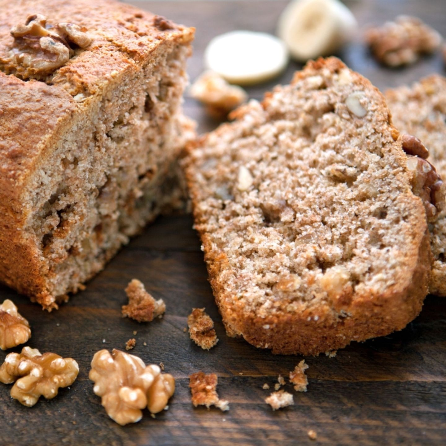 Backen ohne Zucker Aufgeschnittenes Bananenbrot, daneben liegen Bananenscheiben und Walnüsse