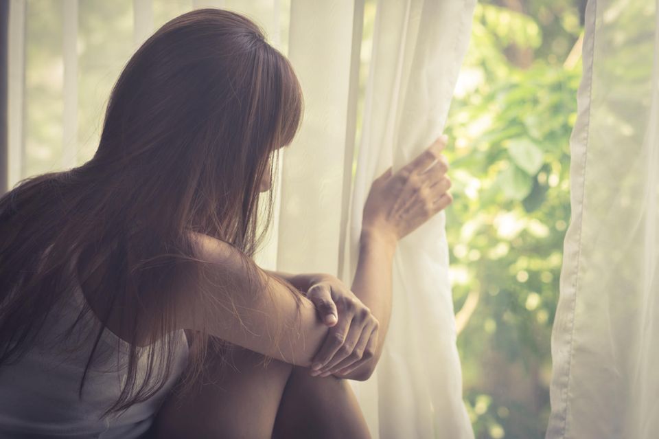 Was kann ich aus einer Krise lernen? Eine traurige Frau schaut durch einen Vorhang nach draußen