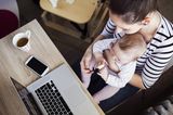 Fläschchen-Mütter: Frau mit Baby auf dem Schoß am Schreibtisch