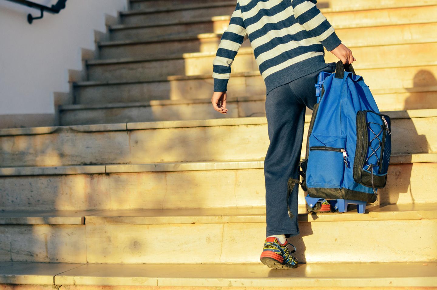 Vereinbarkeit: Junge geht Treppe hoch und trägt seine Schultasche