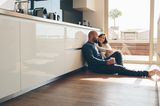 Vereinbarkeit: Eltern sitzen in der Küche auf dem Boden