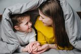 Schlafprobleme bei Babys und Kleinkindern: Mutter kuschelt mit Kind unter Bettdecke