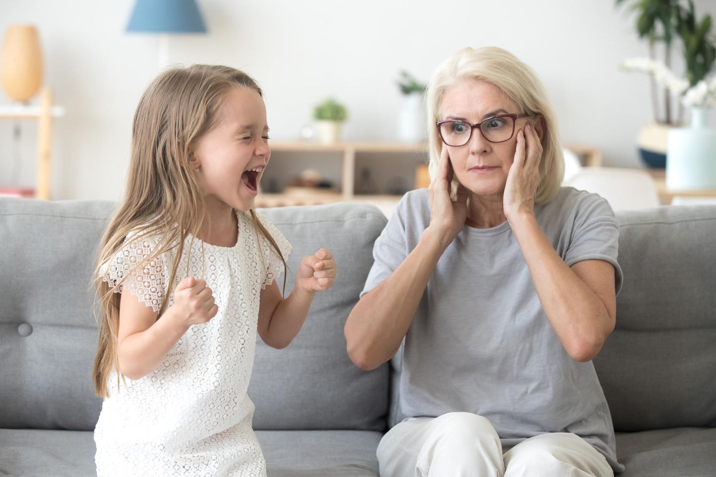 Trotz: Großmutter hält sich die Ohren zu während kleines Mädchen schreit