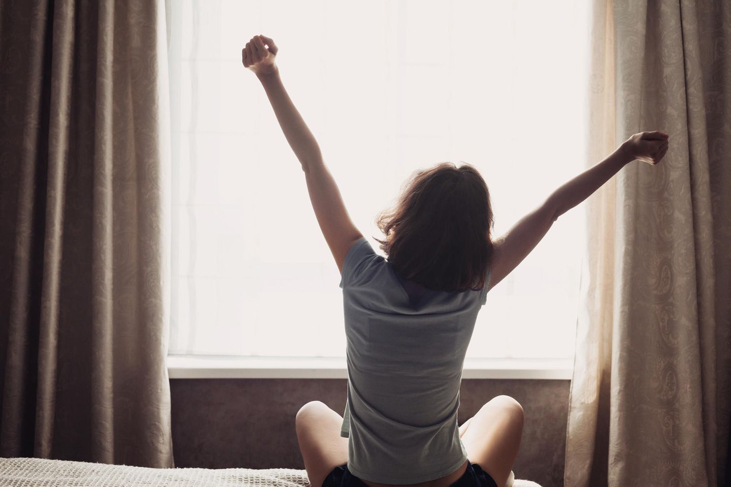 Morgenrituale erfolgreicher Menschen: Eine Frau sitzt auf ihrem Bett und streckt sich