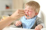 Beikost-Start: Rezepte und Tipps: Weinendes Baby wird mit Brei gefüttert