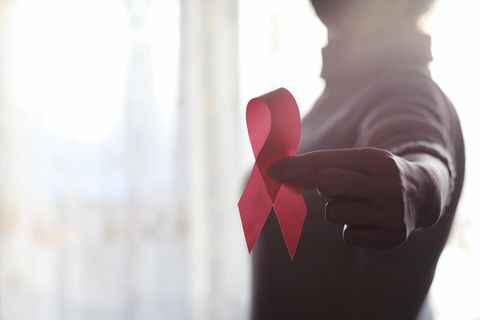 Brustkrebs behandeln: Frau hält rotes Band in die Kamera