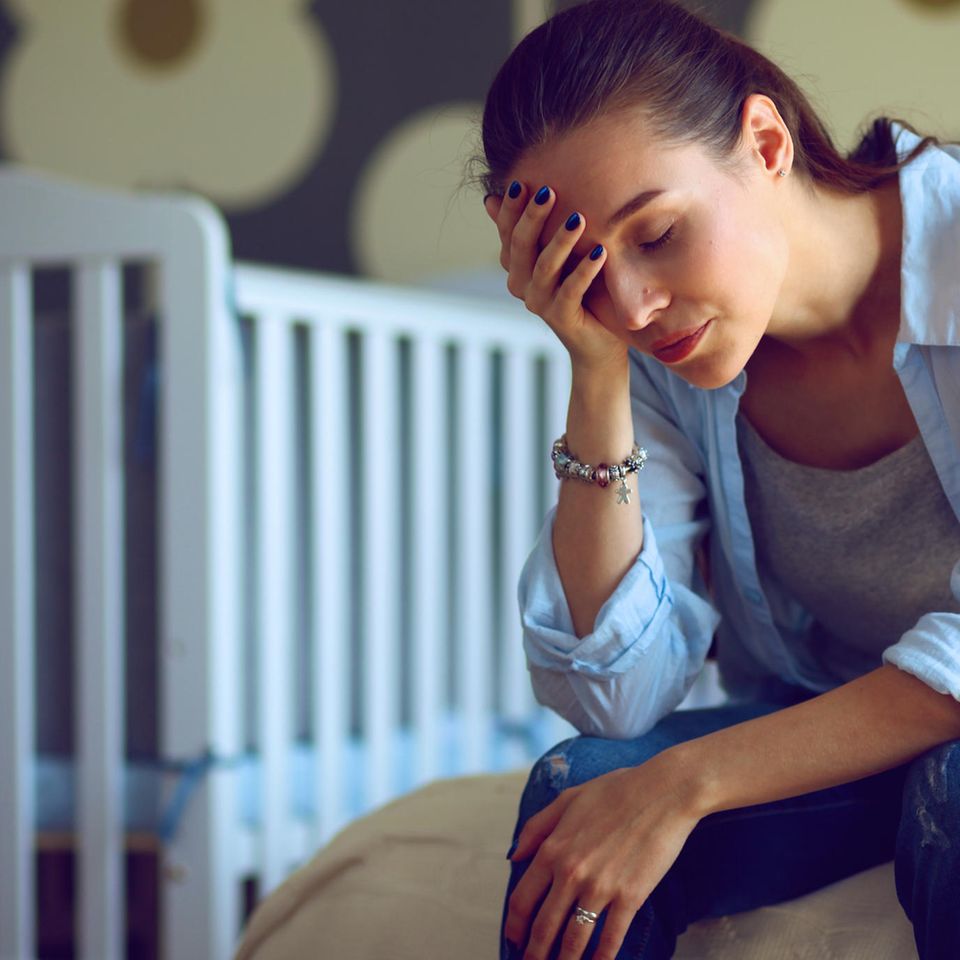 Emotionen im Wochenbett: Erschöpfte Mutter vor Kinderbett