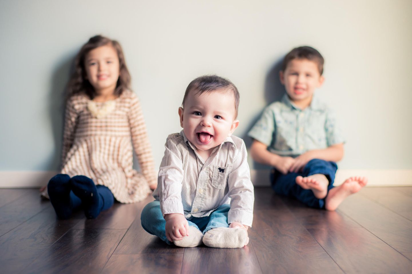 Drittes Kind: Drei Geschwister sitzen auf dem Boden