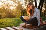 Familienleben: Frau liest draußen auf Bank