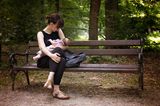 Stillen: Mutter stillt Baby auf der Parkbank