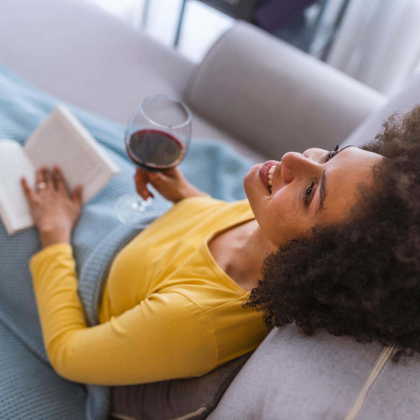Schlechte Mutter? So ein Quatsch!: Frau sitzt mit Weinglas und Buch auf Couch
