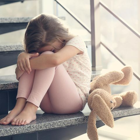 Familienleben: Kind sitzt traurig auf Treppe