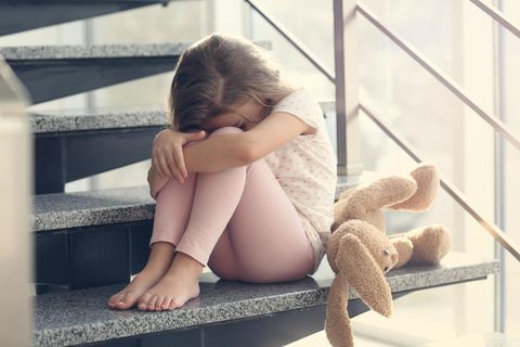 Familienleben: Kind sitzt traurig auf Treppe