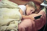 Medienerziehung: Kind mit Handy im Bett