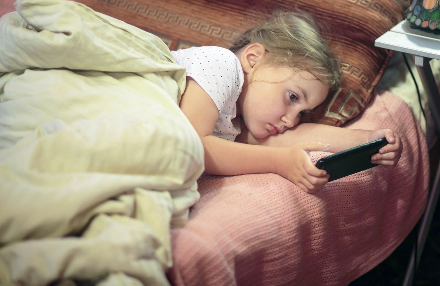 Medienerziehung: Kind mit Handy im Bett