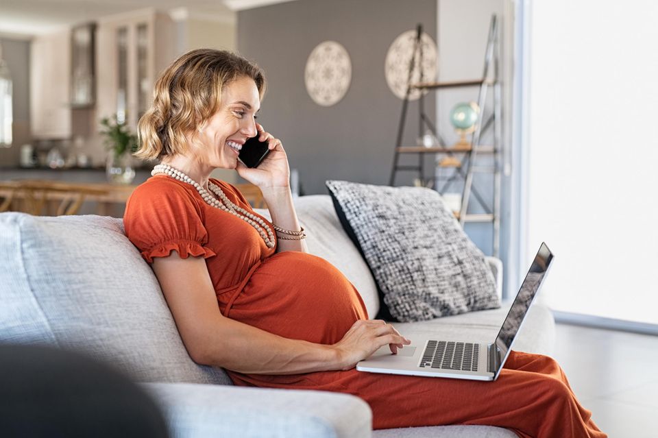 Mehr Geld für die Familie: Schwangere Frau mit Laptop auf der Couch