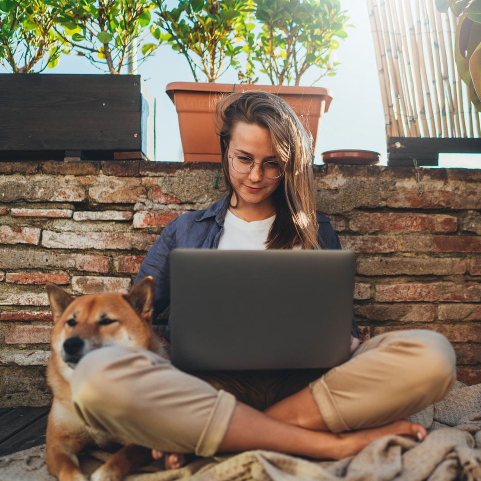 Warum sind manche Menschen so gelassen? Eine entspannte Frau mit Laptop und Hund auf ihrem Balkon